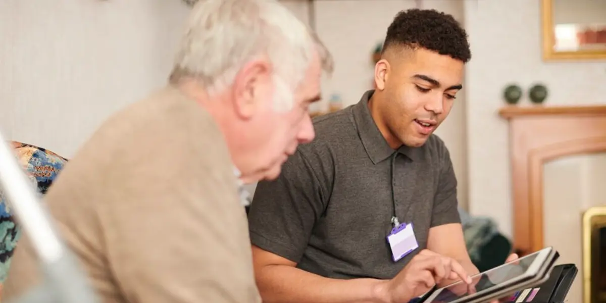 NDIS support worker assisting an elderly man with a digital tablet at home