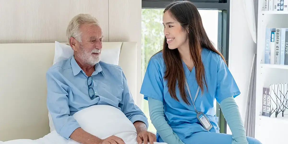 A Registered NDIS Provider offering professional in-home support, with a nurse smiling and assisting an elderly man in a comfortable setting.
