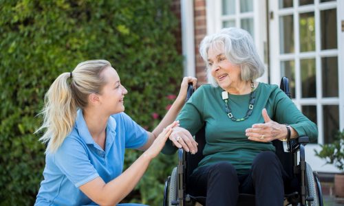 Carer,Pushing,Senior,Woman,In,Wheelchair,Outside,Home